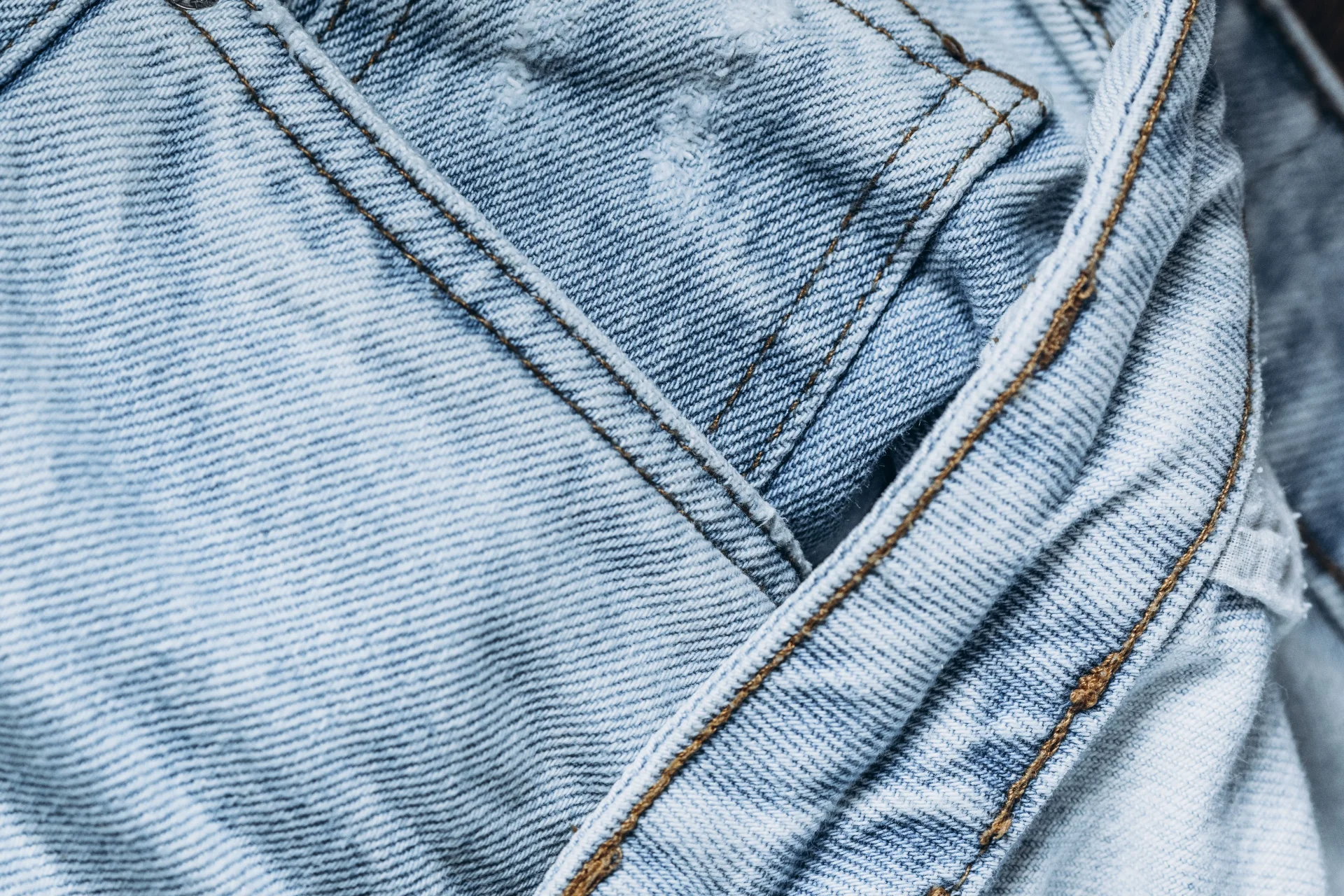 Zbliżenie na jasnoniebieską tkaninę dżinsową z widocznymi szwami i teksturą materiału.